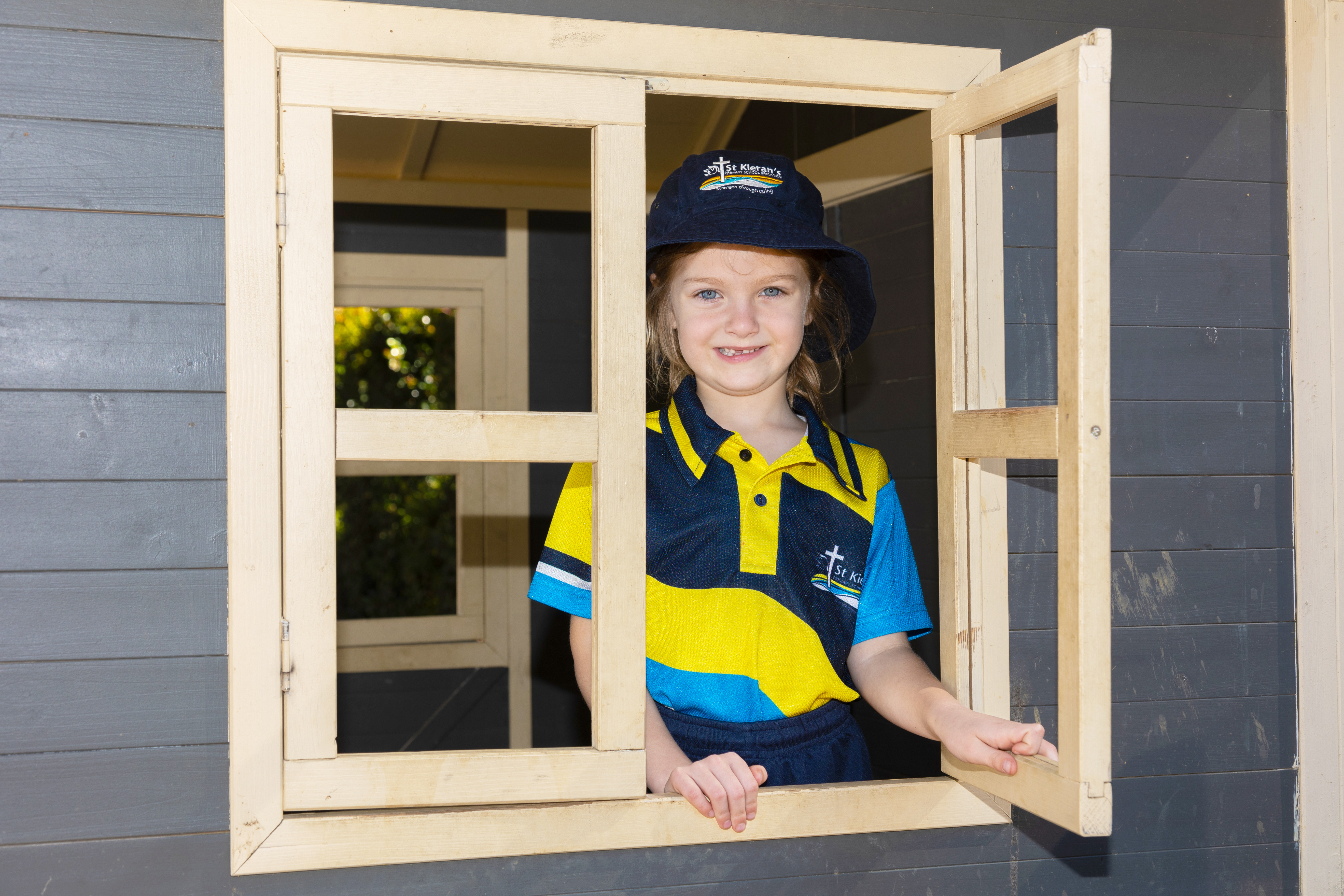 Student in school uniform smiling and leaning through an open window of a wooden play structure